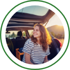 A young woman sits in the open trunk of a SUV and smiles.